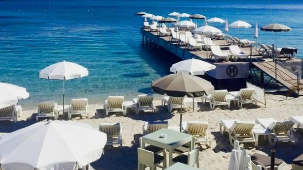 A beachside resort with sun loungers and umbrellas, a pier extending into the sea, and mountains in the background. - T2 new, cap d'antibes, very comfortable, terrace, air conditioning, PK (Antibes)