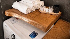 A bathroom with a white washing machine, neatly folded towels, and toiletries on a wooden tray.