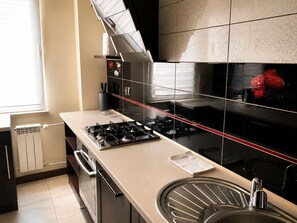 A modern kitchen with a gas stove, a stainless steel sink, and a black backsplash. - BAIO Apart Sapphire (Libiaz)
