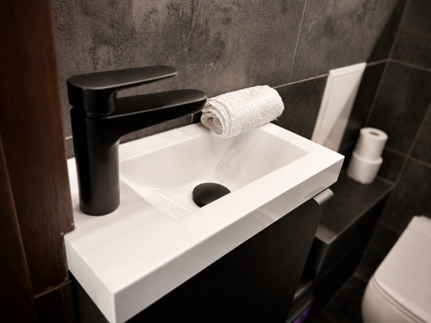 A modern bathroom with a white sink, black faucet, and a towel dispenser.