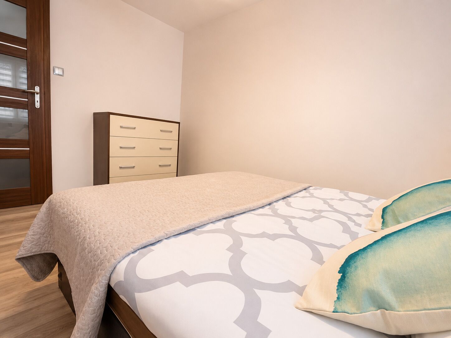 Un dormitorio con cama, un armario de madera y una puerta con paneles de vidrio esmerilado.