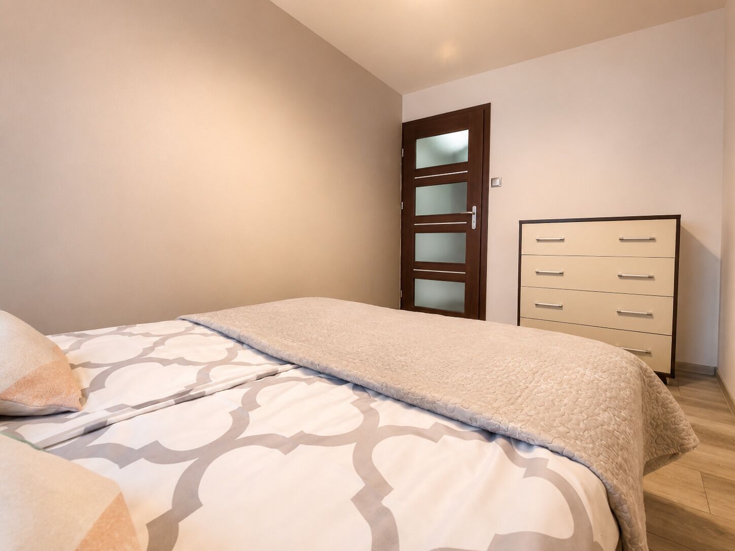 Une chambre à coucher comprenant un lit, une commode et une porte dont les panneaux sont en verre dépoli.