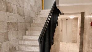 A modern staircase with marble steps and a black handrail, leading to a door at the top.