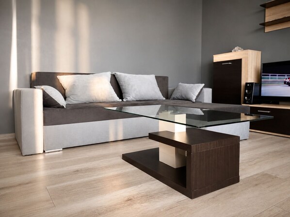 A modern living room with a sofa, a glass coffee table, and a TV.