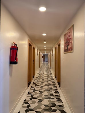Un pasillo de hotel con piso de diseño geométrico, puertas de madera y un extintor de incendios colgado en la pared.