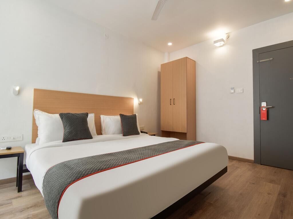 A hotel room with a large bed, a wardrobe, a desk, and a door.