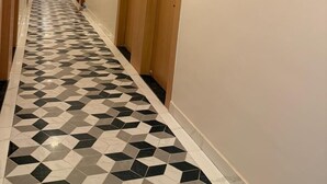 Un pasillo de hotel con piso de diseño geométrico, puertas de madera y un cuadro de flores en la pared.