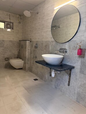 Un baño con un inodoro blanco, un espejo redondo, un lavamanos blanco sobre una encimera negra y una zona de ducha.