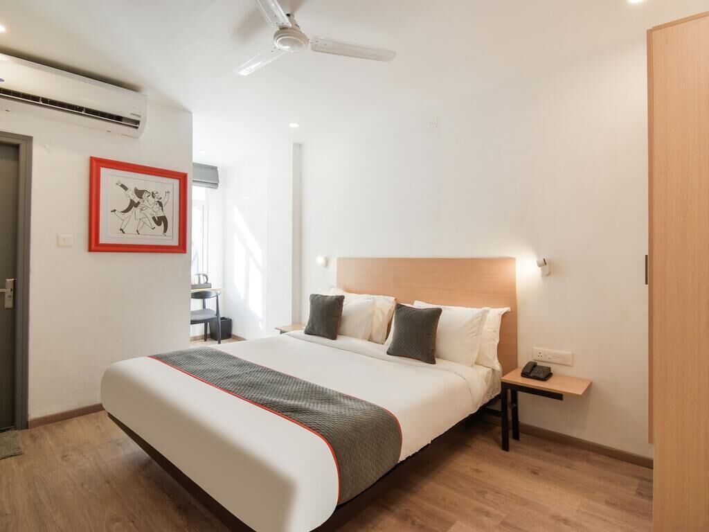 A hotel room with a large bed, a bedside table, a nightstand, a ceiling fan, and a framed picture on the wall.