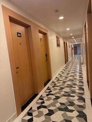Ein Hotelgang mit Holztüren mit den Nummern 301 und 302, einem Schachbrettfußboden und eingelassenen Deckenleuchten.