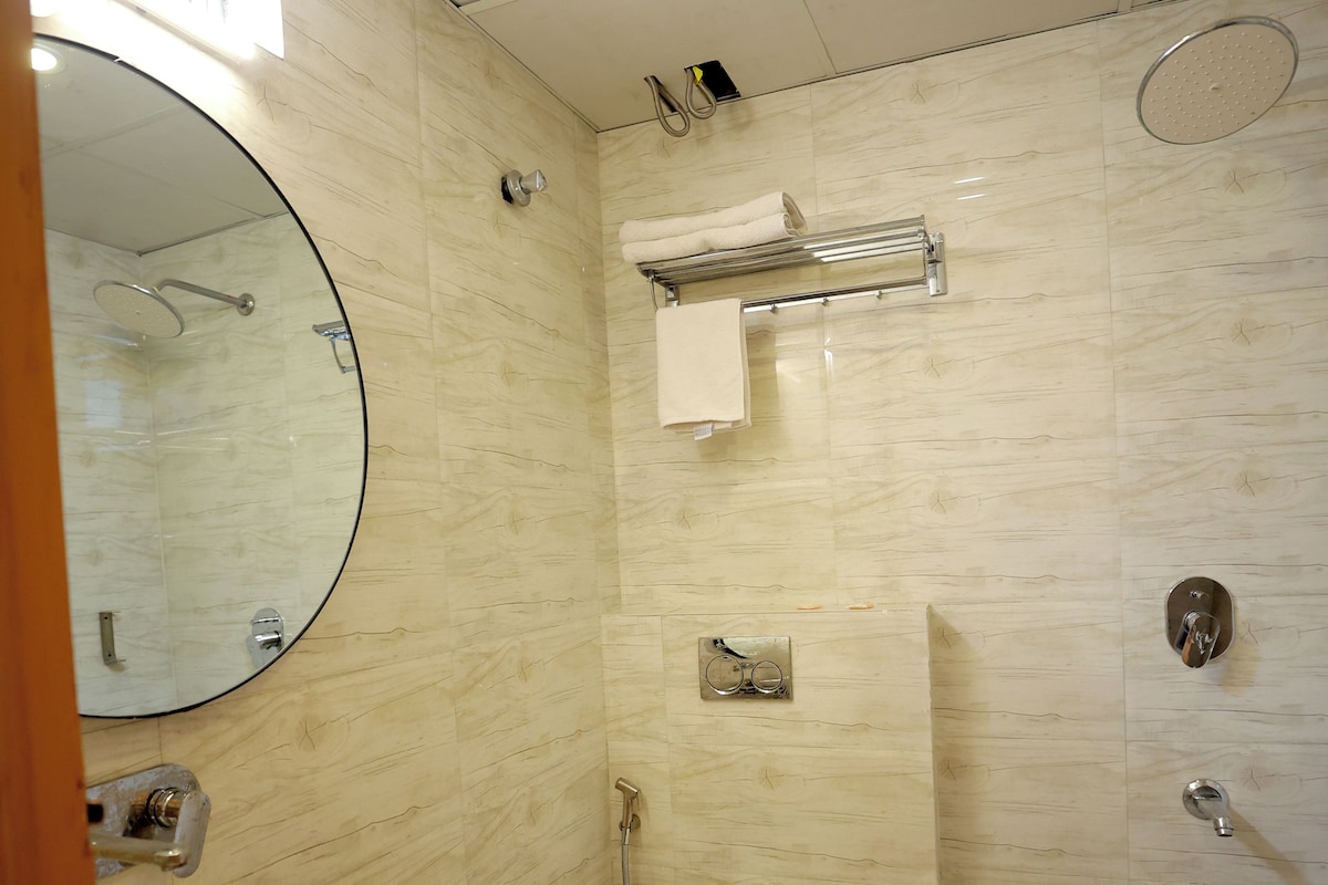 Une salle de bain avec un grand miroir rond, deux lavabos, des toilettes, une douche et un porte-serviettes.