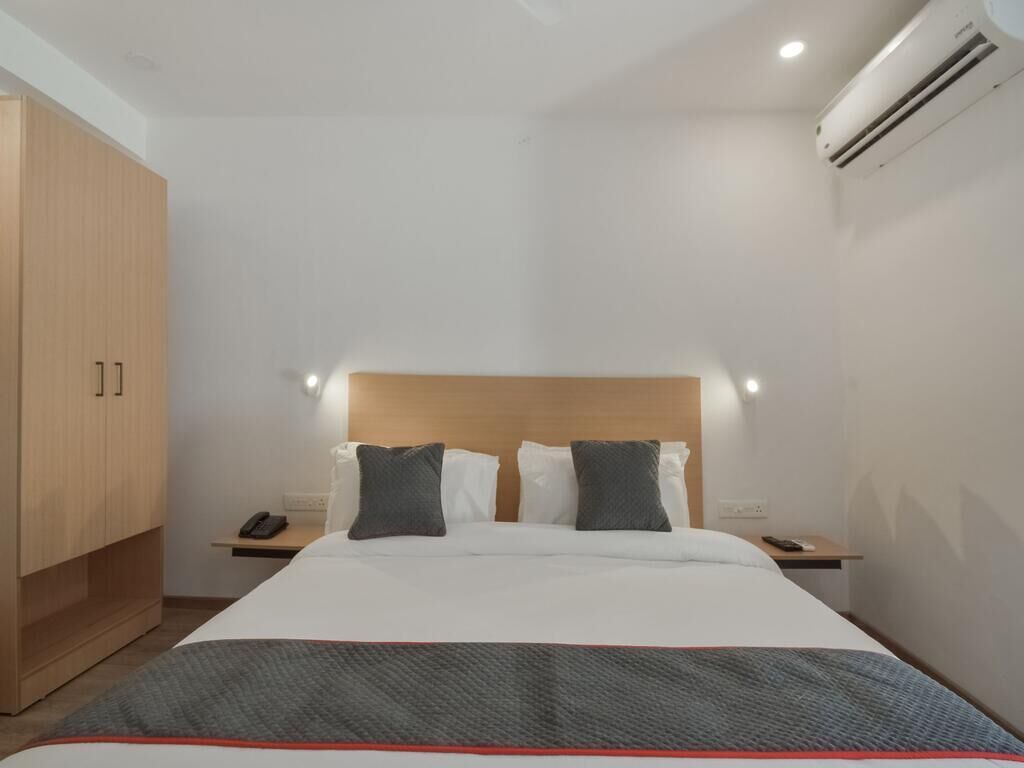 A hotel room with a bed, bedside tables, a wardrobe, and an air conditioning unit.