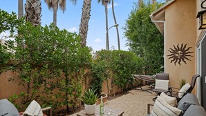 A patio with outdoor furniture, a potted plant, and a wall-mounted sun decoration. - Perfect Mesa Retreat | Remodeled Condo with a Pool (Santa Barbara)