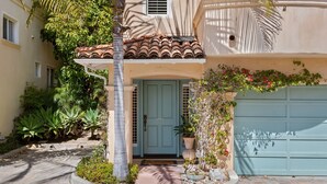 A two-story house with a light blue door, a tiled roof, and a garage door. - Perfect Mesa Retreat | Remodeled Condo with a Pool (Santa Barbara)