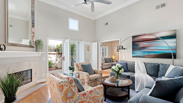 A spacious living room with a fireplace, a ceiling fan, and a large painting. - Perfect Mesa Retreat | Remodeled Condo with a Pool (Santa Barbara)