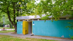A portable restroom with a yellow door, located next to a green wall and a tree. - Munich Central Camping (Munich)
