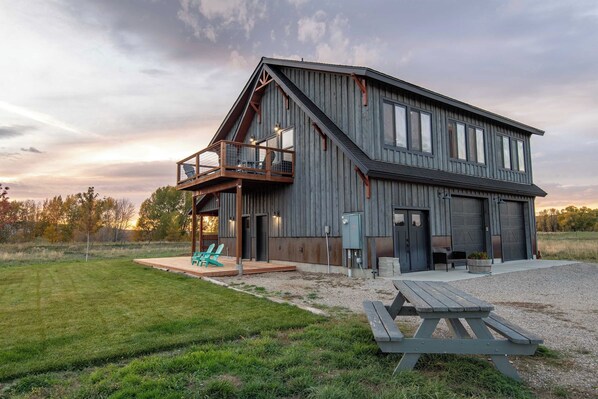 A large, two-story wooden house with a balcony, a covered porch, and a gravel driveway.
