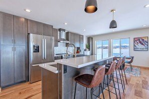 A modern kitchen with stainless steel appliances, a large island with bar stools, and a view of mountains through the windows.