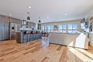 A modern kitchen with a central island, bar stools, and a large window overlooking a snowy landscape.