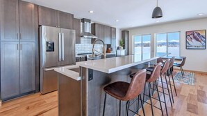A modern kitchen with stainless steel appliances, a large island with bar stools, and a view of mountains through large windows.