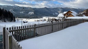 A snow-covered landscape with a wooden fence, a wooden house with snow on the roof, and mountains in the background. - Kumitzblick: A Modern, High-End Vacation Rental (Pichl-Kainisch)
