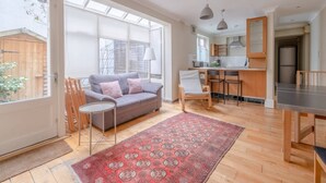 A spacious living area with a sofa, a dining table, and a kitchen in the background. - Lovely 1 Bedroom With Patio - 10 Mins From Hyde Park (London)