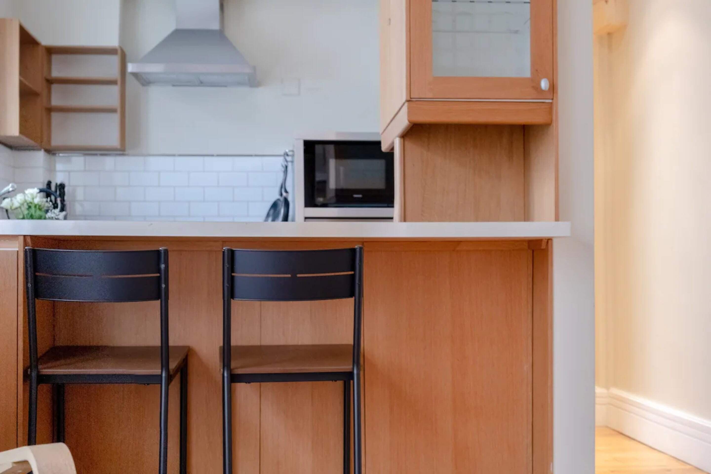 A kitchen with wooden cabinets, a microwave, and two black chairs.