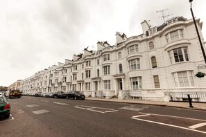 A row of white townhouses with uniform architecture, a clear road, and parked cars.