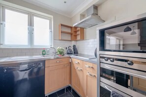 A modern kitchen with a dishwasher, oven, and wooden cabinets. - Lovely 1 Bedroom With Patio - 10 Mins From Hyde Park (London)