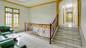 A staircase with a red railing leading to an upper floor, a green sofa, and a window with yellow frames. - Hotel O Penginapan Aina Syariah (Lebaho Ulaq)
