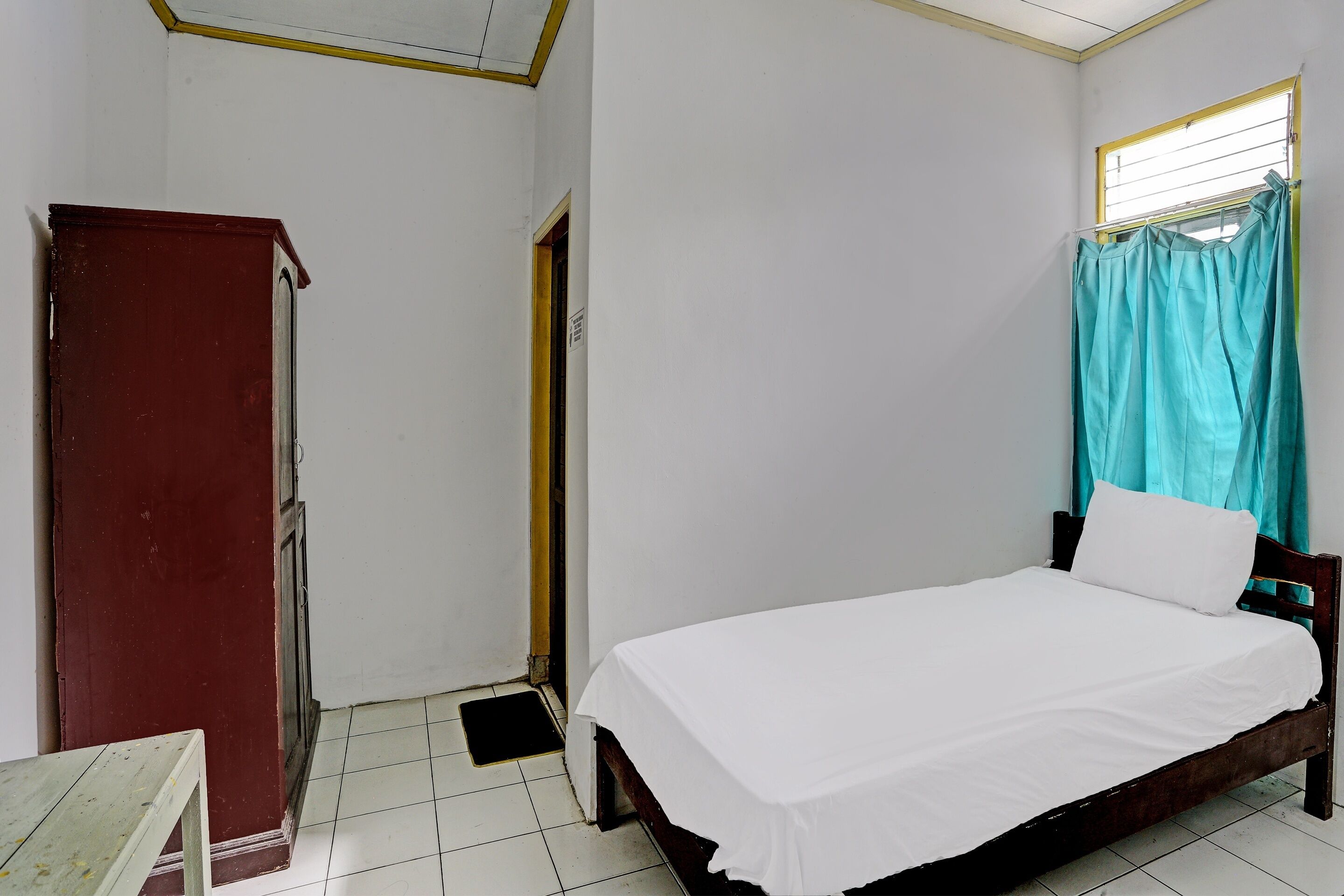 Una habitación con una cama individual, un armario de madera, una mesita pequeña y una ventana con cortinas.