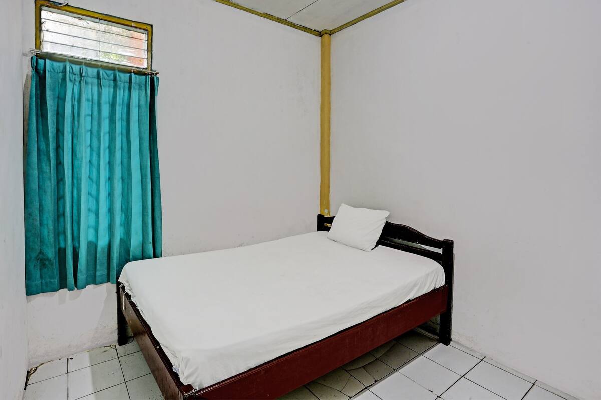 A single bed with a wooden frame and white bedding in a room with white walls and a tiled floor.