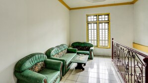 A room with a green sofa set, a small table, and a window with yellow frames. - Hotel O Penginapan Aina Syariah (Lebaho Ulaq)