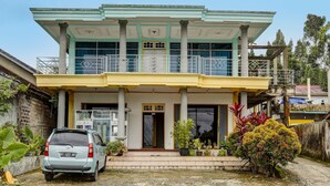 A two-story building with a balcony, a car parked in front, and various potted plants. - Hotel O Penginapan Aina Syariah (Lebaho Ulaq)