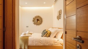 A bedroom with a wooden bed, white bedding, a woven rug, and a wall-mounted mirror. - Vale Lobo Golf & Beach with Private Pool II (Almancil - VALE DO LOBO)