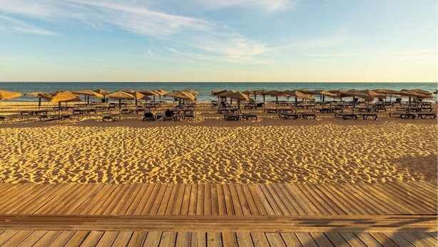 A beach with wooden deck chairs and umbrellas, a sandy beach, and the ocean in the background. - Vale Lobo Golf & Beach with Private Pool II (Almancil - VALE DO LOBO)