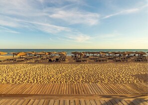 Une plage avec des chaises longues et des parasols en bois, une plage de sable, et l’océan en arrière-plan.