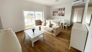 Un salon moderne avec un canapé beige, une table basse blanche et un coin repas comprenant une table et des chaises blanches.