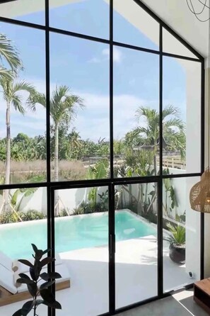 A room with large windows overlooking a swimming pool and lush greenery. - Villa Tala (Canggu)