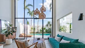 Un salón moderno con un gran ventanal, un sofá verde, muebles de madera y vistas a una piscina.
