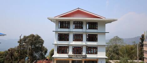 A multi-story hotel with a red roof and white walls, featuring a sign that reads "Sikkim Sarovar Hotel & Resort."