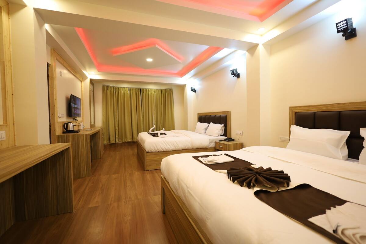A hotel room with two beds, a TV, a desk, and a wooden floor.