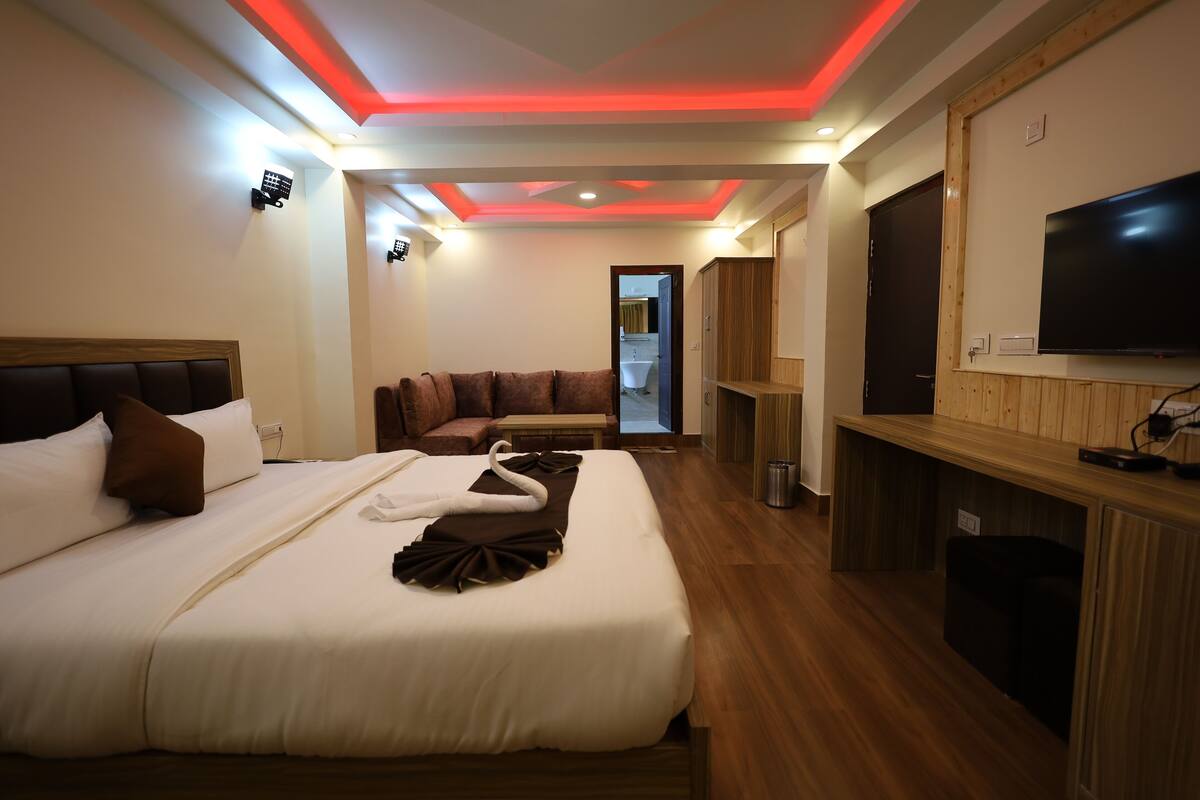 A hotel room with a large bed, a TV, a wooden cabinet, and a mirror.