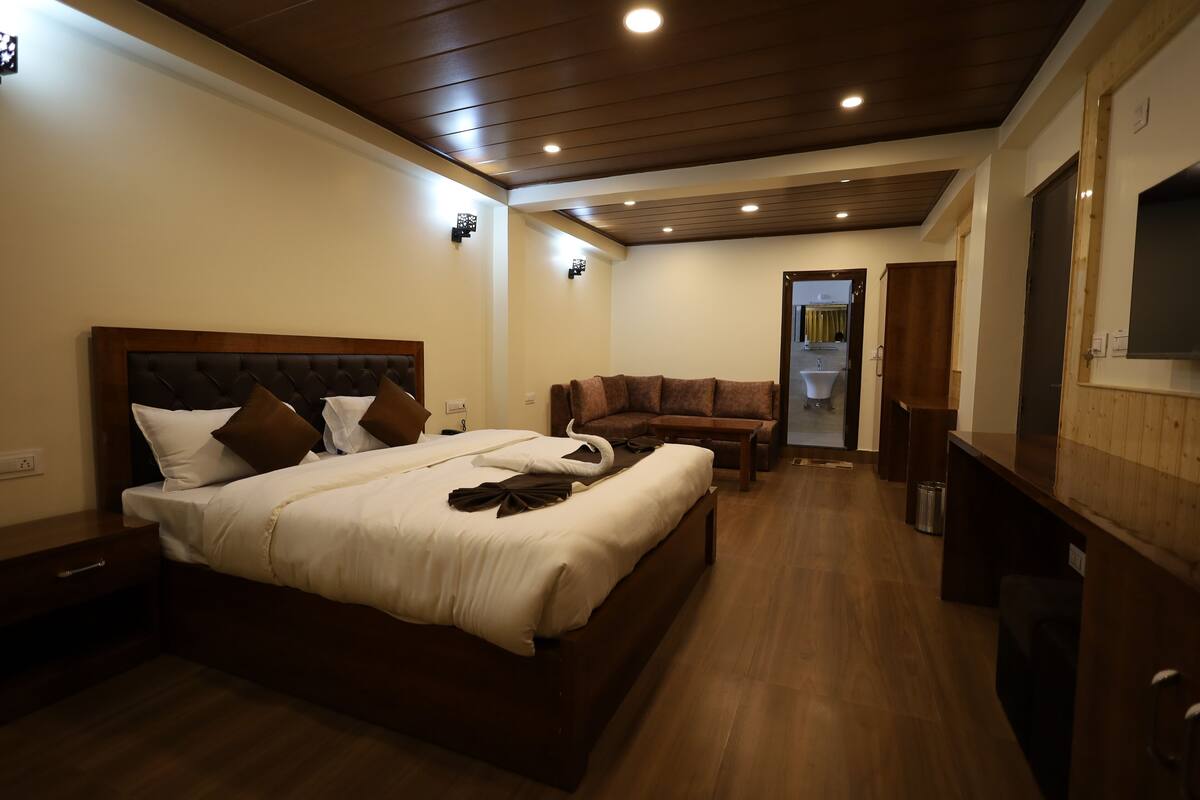 A hotel room with a large bed, a wooden headboard, a sofa, and a TV mounted on the wall.