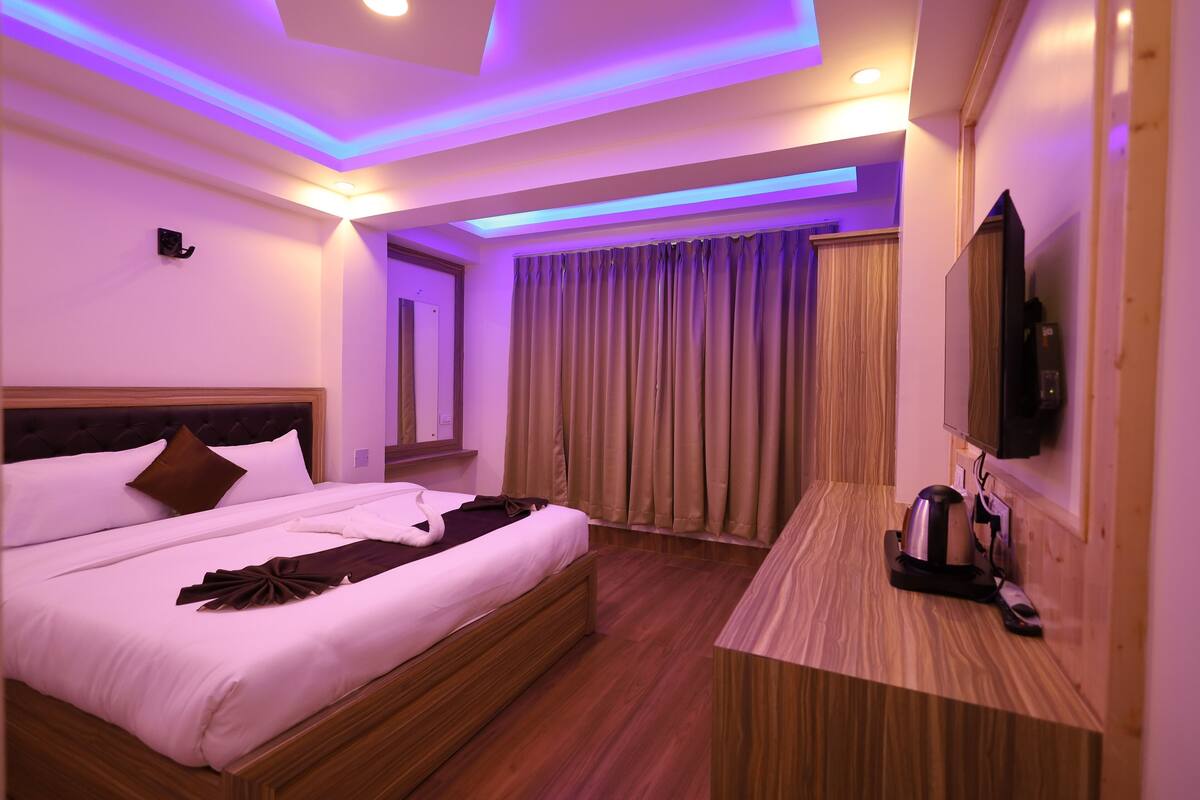 A hotel room with a bed, a desk, a television, and a window with curtains.