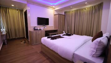 Habitación de hotel con una cama grande, un televisor de pantalla plana montado en la pared, armarios de madera y una mesita con hervidor y tazas.