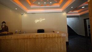 A reception desk with a wooden finish, a neon sign above it, and a Buddha statue to the left. - Sikkim Sarovar (Namchi)