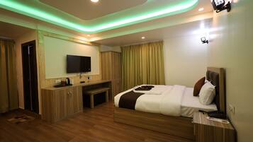 A modern hotel room with a wooden floor, a bed with white bedding, a TV mounted on the wall, and a desk with a chair.
