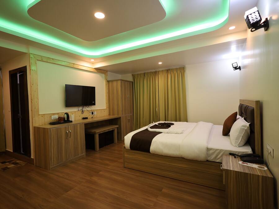 A modern hotel room with a wooden floor, a bed with white bedding, a TV mounted on the wall, and a desk with a chair.