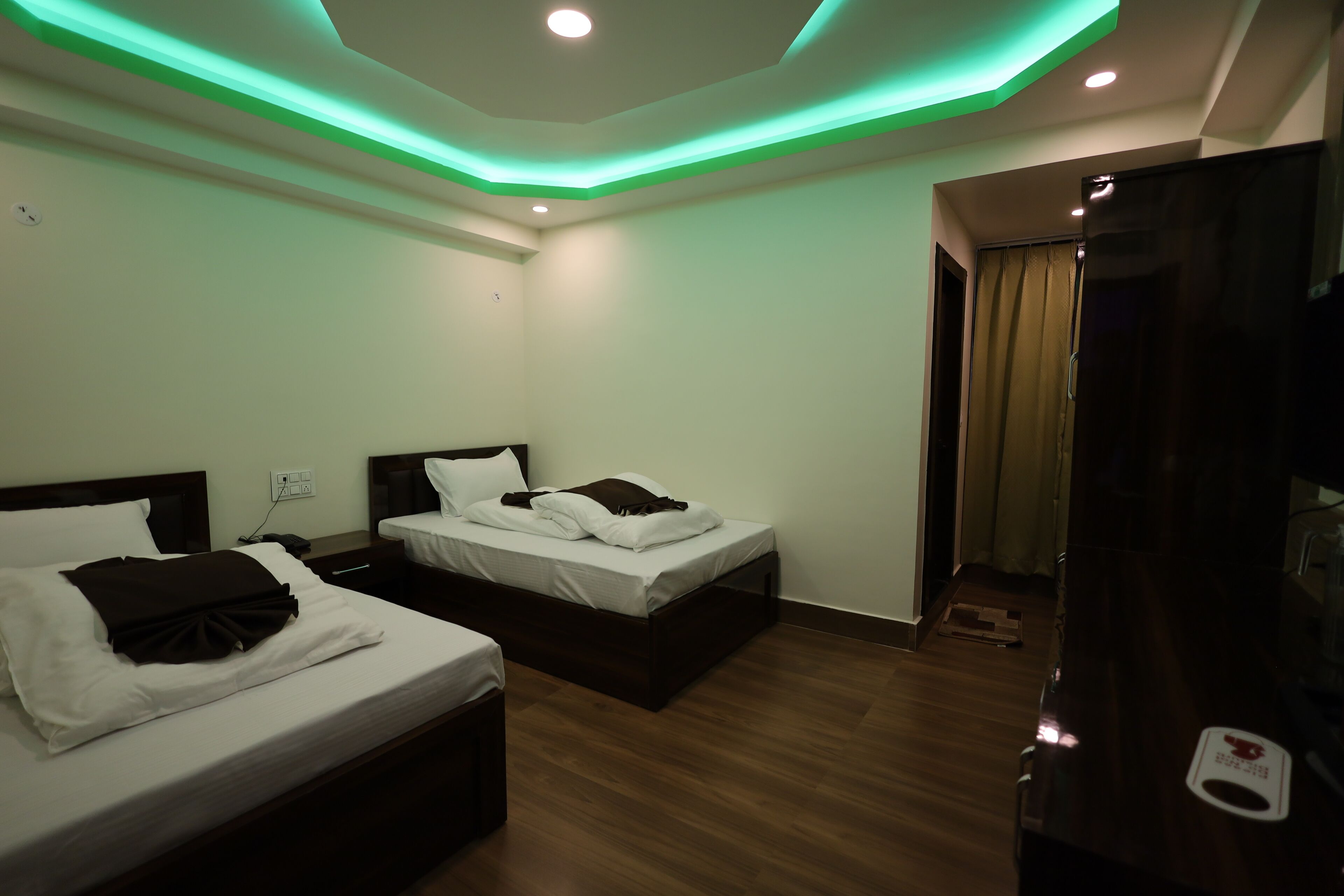 A hotel room with two beds, wooden flooring, and green ambient lighting.